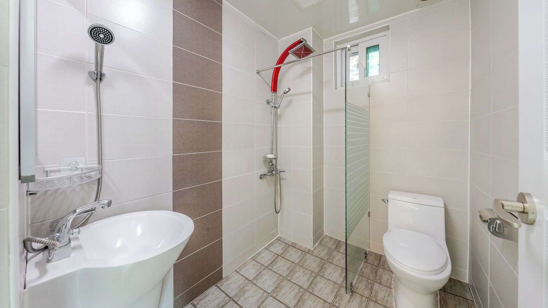 A bathroom with a white sink, a shower with a red head, and a toilet.