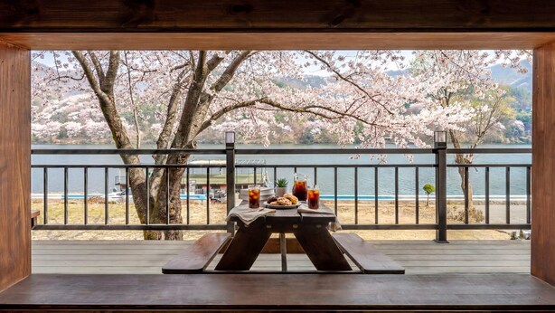 A wooden deck with a picnic table, a view of a lake, cherry blossoms, and a distant shoreline. - Gapyeong Eos Pension (Gapyeong)