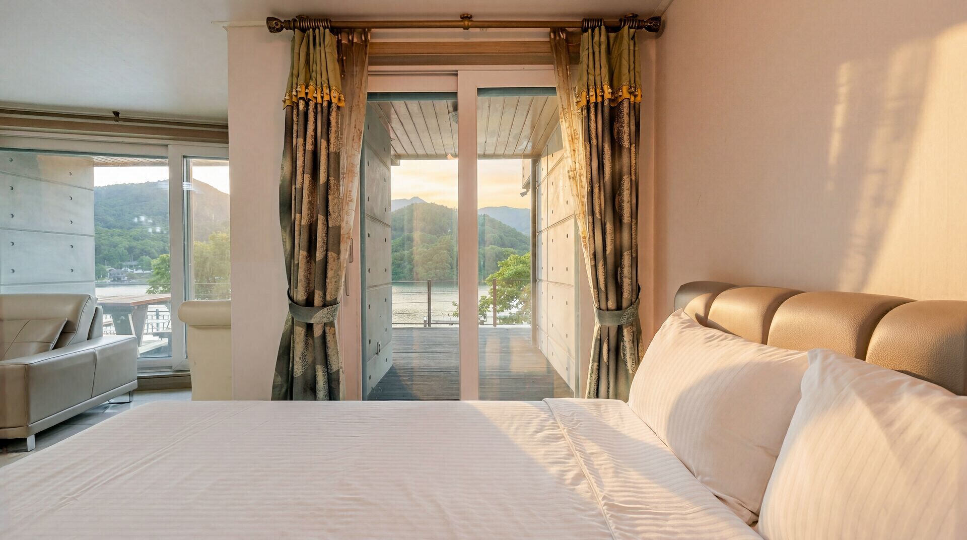 A bedroom with a bed, a view of a lake, and a balcony with curtains.