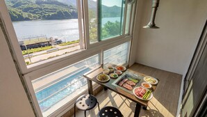 A balcony with a table set for a meal, a pool, and a view of a lake and mountains. - Gapyeong Eos Pension (Gapyeong)