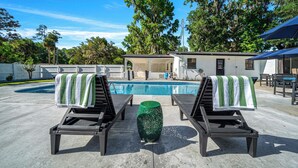 Zona de piscina con sillones de descanso, una mesita y un edificio al fondo.