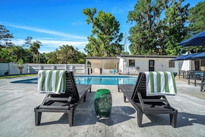 A poolside area with lounge chairs, a small table, and a building in the background. - Private suite with pool access near WEC, Downtown, Restaurants, Publix & More! (Ocala)