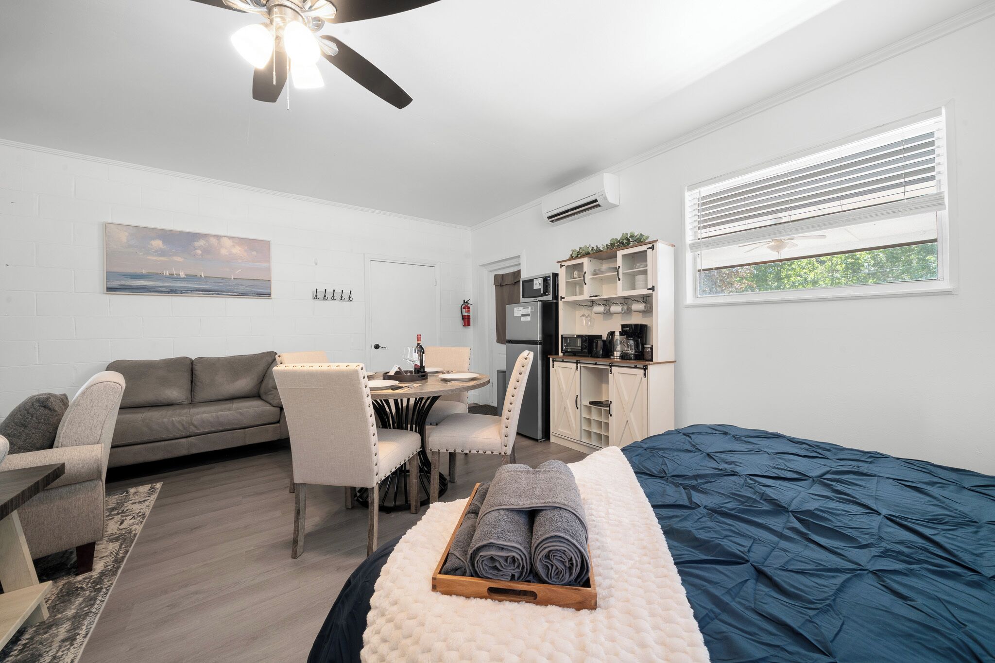 Un dormitorio con cama, escritorio, sillón, sofá y zona de cocina.
