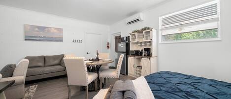 Un dormitorio con cama, escritorio, sillón, sofá y zona de cocina.