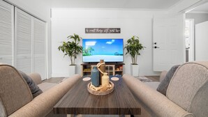 Una sala de estar con televisor, dos plantas en macetas, un centro de mesa decorativo y un sofá.
