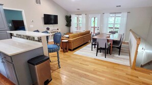 A modern kitchen with a bar area, a dining table with chairs, a sofa, and a staircase. - Stone Landing Lakefront Retreat: Spacious 2-bed, 3-bath House with Private Dock (Fair Play)