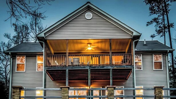A two-story house with a balcony, a central fan, and a stone foundation. - Stone Landing Lakefront Retreat: Spacious 2-bed, 3-bath House with Private Dock (Fair Play)
