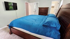 A bedroom with a bed, a dresser, a television mounted on the wall, and a door leading to another room. - Stone Landing Lakefront Retreat: Spacious 2-bed, 3-bath House with Private Dock (Fair Play)