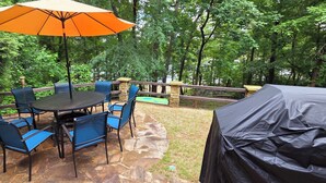 An outdoor patio with a round table and blue chairs, surrounded by stone flooring, and an orange umbrella. - Stone Landing Lakefront Retreat: Spacious 2-bed, 3-bath House with Private Dock (Fair Play)