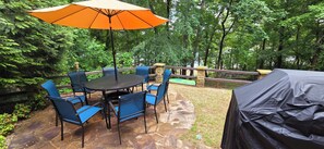 An outdoor patio with a round table and blue chairs, surrounded by stone flooring, and an orange umbrella.