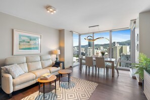 Ein modernes Wohnzimmer mit Sofa, Couchtisch und Essbereich, mit einem großen Fenster und Blick auf die Stadt.