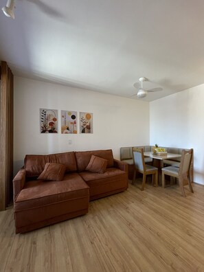 Ein Wohnzimmer mit einem braunen Ecksofa, einem Esstisch mit Stühlen und einem Deckenventilator.