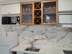 Eine Küche mit Marmor-Spritzschutz, einem Spülbecken und Schränken mit Glastüren, in denen Weingläser aufbewahrt werden.