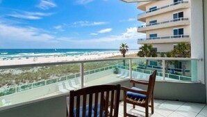 Ein Balkon mit zwei Holzstühlen, Blick auf den Strand und ein Gebäude im Hintergrund.