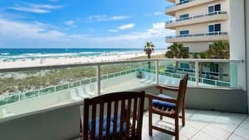 A balcony with two wooden chairs, a view of the beach, and a building in the background.