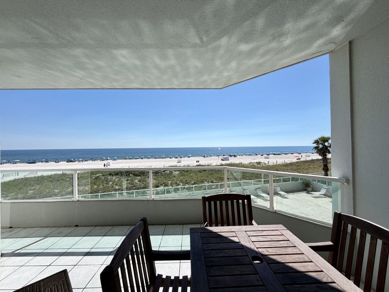 A balcony with a view of the beach, a table, and two chairs.