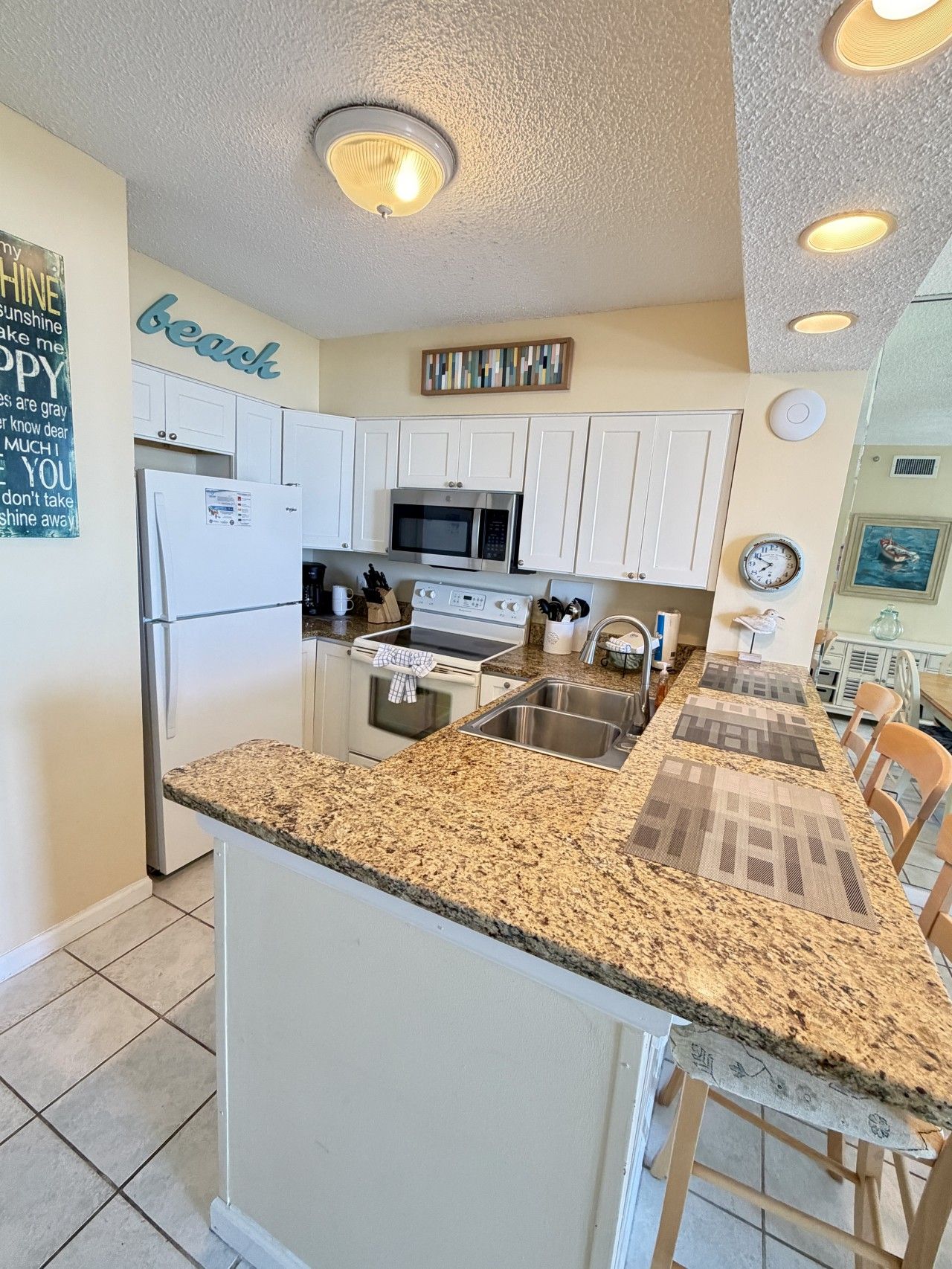 A kitchen with white cabinets, a granite countertop, a microwave, a stove, and a sink.