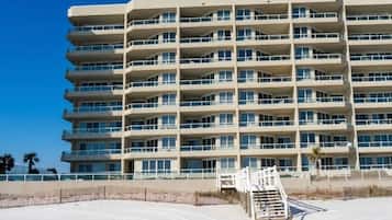 A multi-story hotel with balconies, a sandy beach in the foreground, and a clear blue sky.