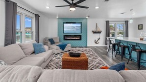 Een moderne woonkamer met een bank, een televisie, een open haard en een keukenhoek met barstoelen.
