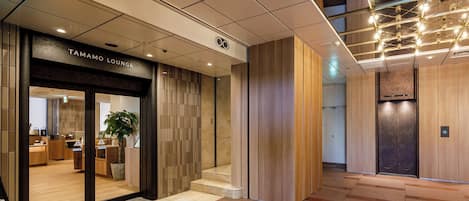 A modern lobby with a Tamamo Lounge entrance, a wooden panel wall, and a tiled floor.