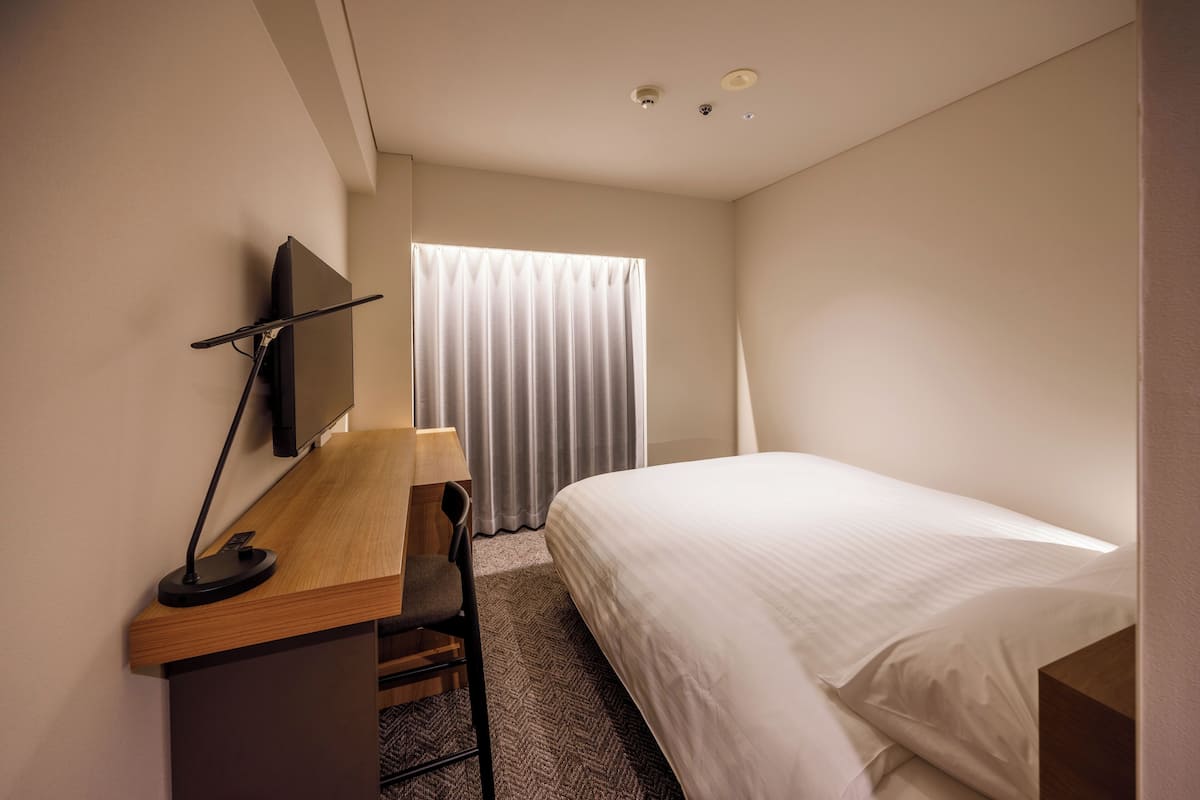 Een hotelkamer met een bed, een bureau met stoel, een televisie en een raam met gordijnen.