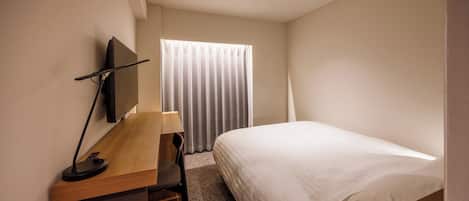 Una habitación de hotel con una cama, un escritorio con silla, televisor y ventana con cortinas.