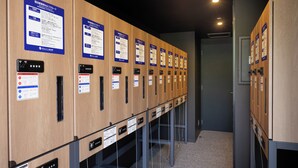 A row of wooden lockers with informational signs, a control panel, and a door in the background. - JR Clement Inn Takamatsu Hyogomachi (Takamatsu)