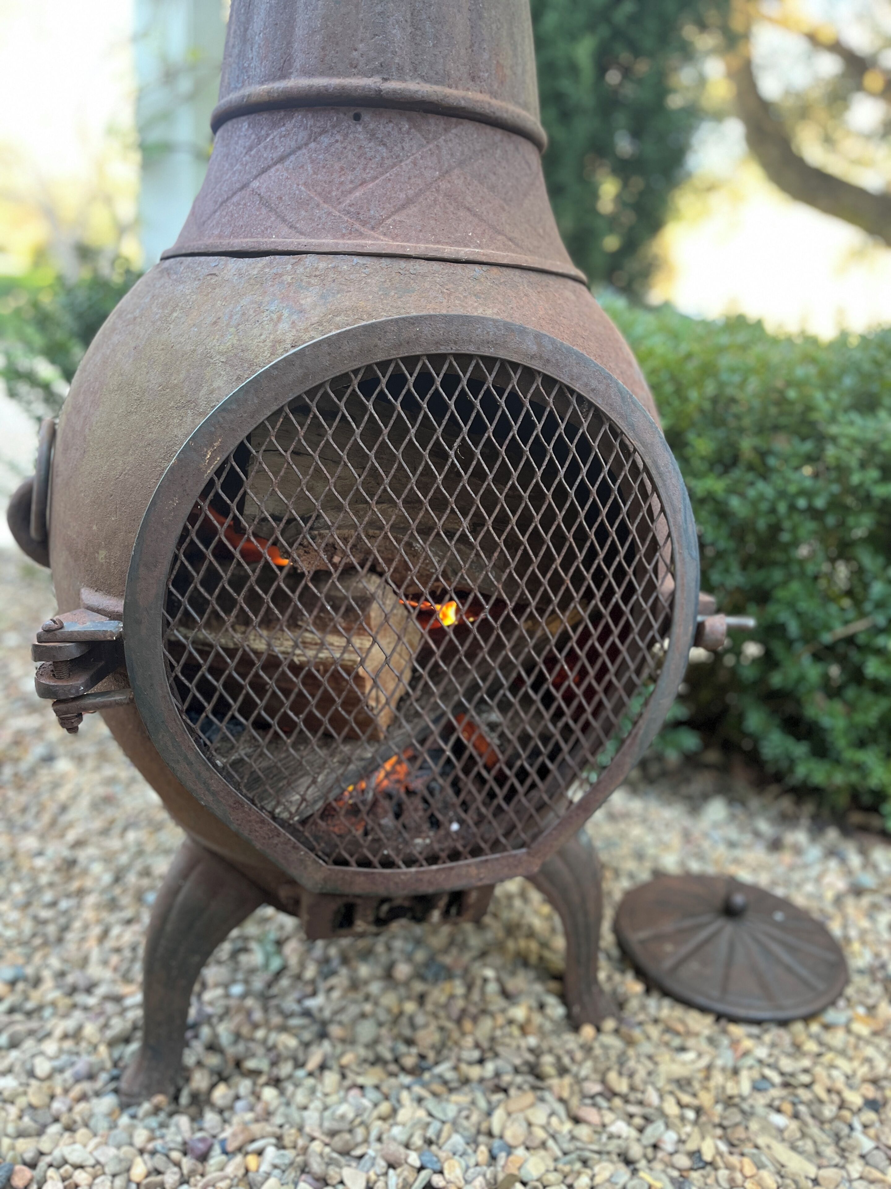 Una parrilla metálica para exteriores con frente de malla, sobre una superficie de grava.