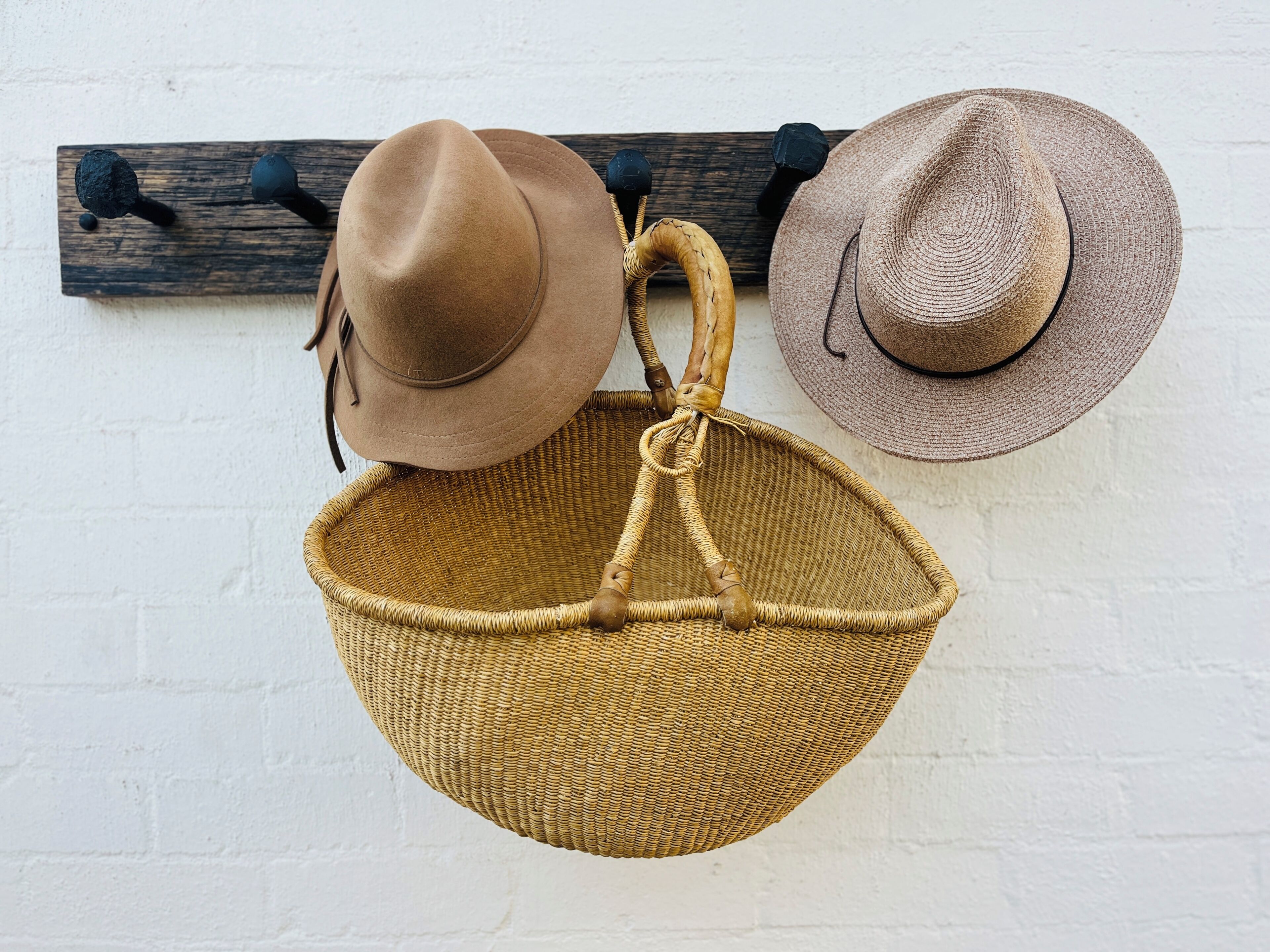 A wall-mounted hat rack with two hats and a woven basket.