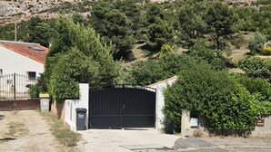 Un barrio residencial con un acceso cerrado, un edificio blanco y una colina con vegetación escasa.