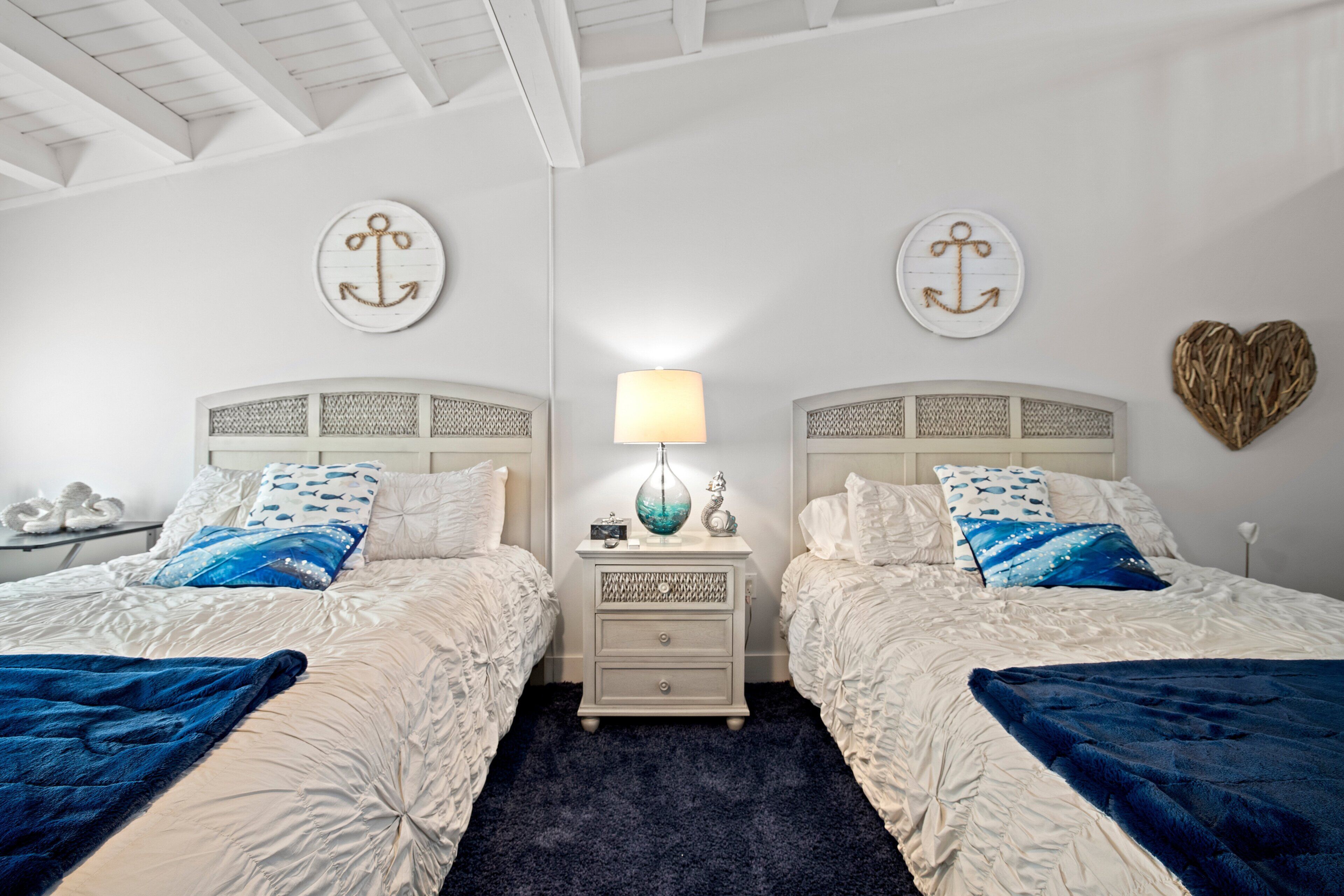 A double bed with a dark blue blanket, a bedside table with a lamp, and two decorative pillows.