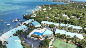 Vista aérea de um resort com vários edifícios, piscina, quadras de tênis e marina com barcos.