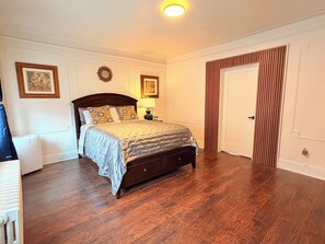 A bedroom with a wooden bed, a nightstand, a lamp, and a door with vertical blinds.