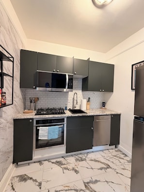 Une cuisine moderne avec des meubles de couleur sombre, une cuisinière en acier inoxydable, un four à micro-ondes et un lave-vaisselle.