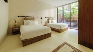Quarto moderno com duas camas, uma pequena mesa de cabeceira com abajur e uma janela grande com vista para o verde.