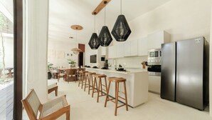 Uma cozinha moderna com uma ilha central, banquetas de bar, uma área de refeições com mesa de madeira e uma geladeira grande.