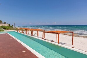 A swimming pool with wooden loungers and a beach view. - Modern Ocean Front 2 BR by BT Homes (Balam Canché)