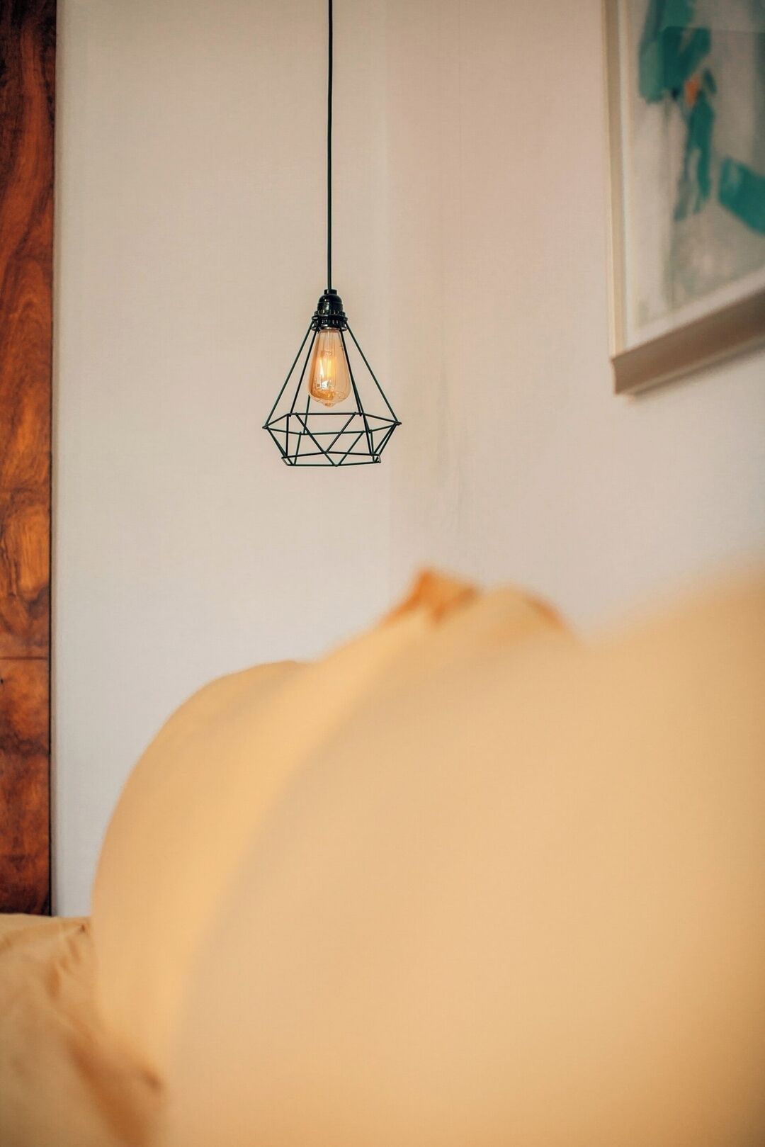 En säng med en vit sänggavel, en hängande lampa och en tavla på väggen.