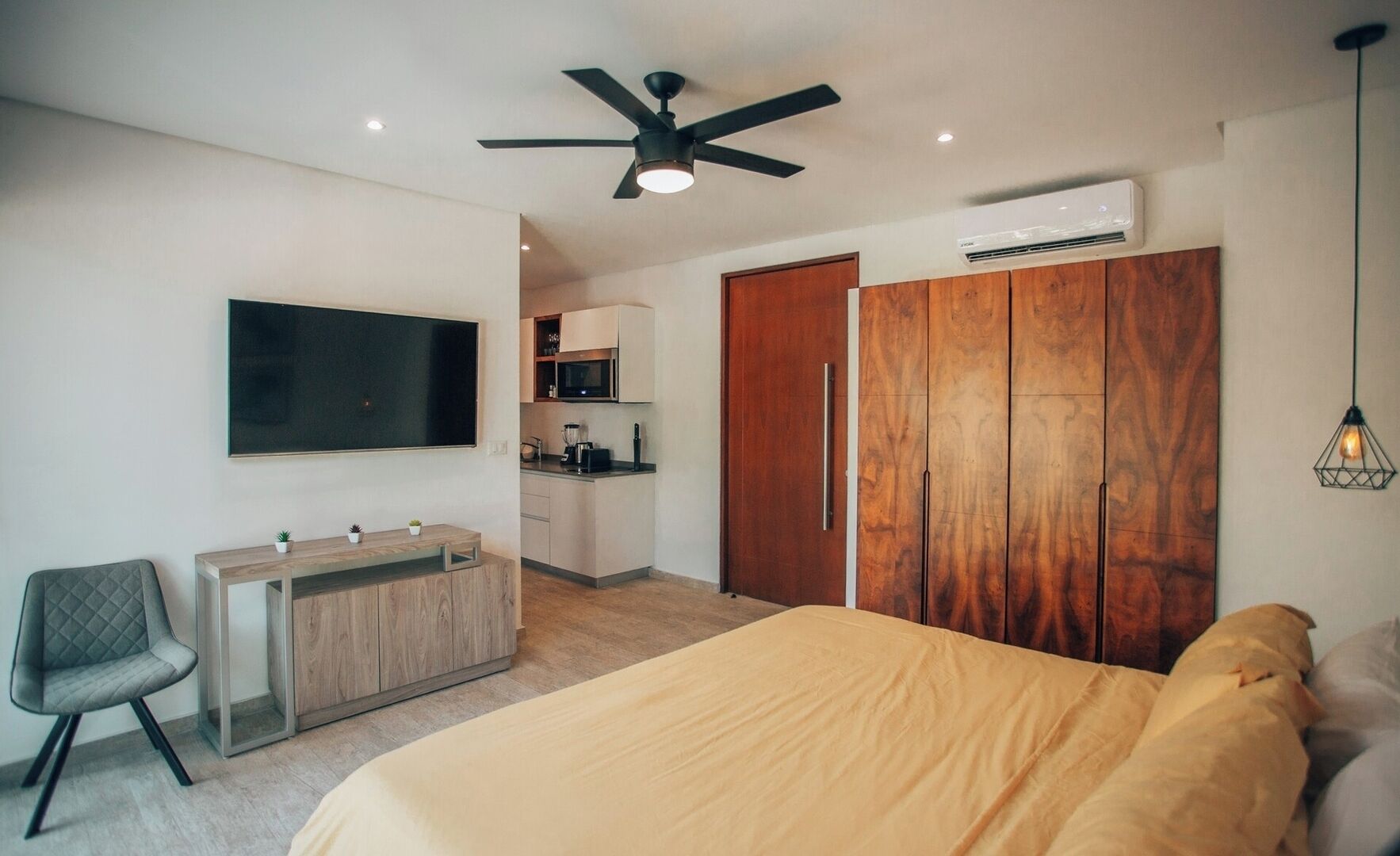 Een slaapkamer met een bed, een bureau, een stoel, een kledingkast, een televisie en een plafondventilator.