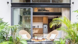 Et moderne hus med store vinduer, en patio med fletningsmøbler og frodig beplantning.