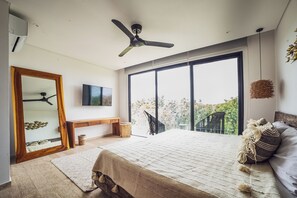 A bedroom with a bed, a ceiling fan, a TV, a large window, and a view of greenery outside. - Selvatico PH and private pool by BT Homes (Tulum)