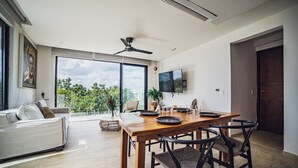 A modern living room with a dining area, large windows, a ceiling fan, and a flat-screen TV. - Selvatico PH and private pool by BT Homes (Tulum)