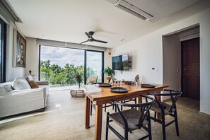 A modern living room with a dining area, large windows, a ceiling fan, and a flat-screen TV. - Selvatico PH and private pool by BT Homes (Tulum)