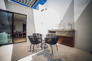 A modern patio with a glass door leading to an interior space, a small dining area with chairs, and a kitchen counter with a sink. - Selvatico PH and private pool by BT Homes (Tulum)