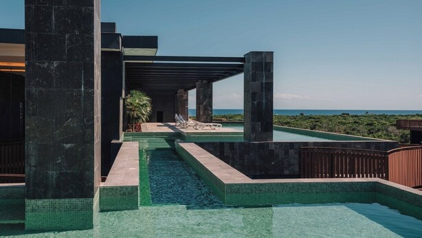 Zona de piscina exterior moderna amb aigua blava cristal·lina, envoltada de murs de pedra i vistes a l'oceà.