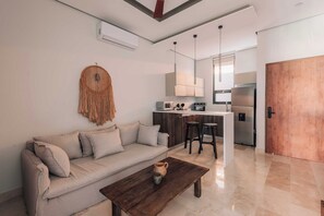 A modern living room with a sofa, coffee table, and kitchen area in the background. - BT Homes - Stylish apartment near the sea (Tulum)