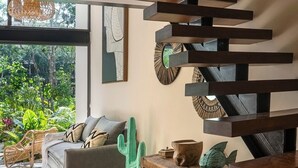 Un intérieur moderne avec un escalier en colimaçon, un canapé gris et une vue sur la verdure à l’extérieur.