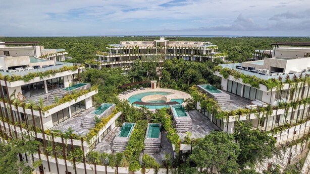Une piscine circulaire, entourée de plusieurs bâtiments dotés de balcons, le tout noyé dans une végétation luxuriante.