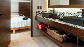 Een moderne badkamer met een grote spiegel, een houten wastafelmeubel, en een bed in de aangrenzende kamer.