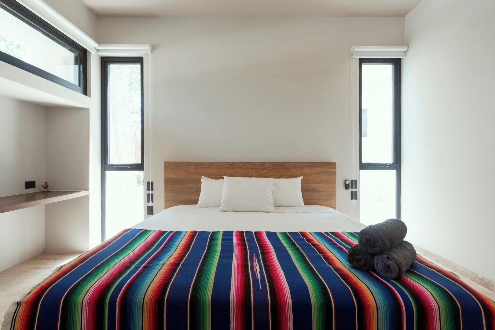 Una camera da letto moderna con una testiera in legno, una coperta a letto a righe colorate e un asciugamano arrotolato sul letto.
